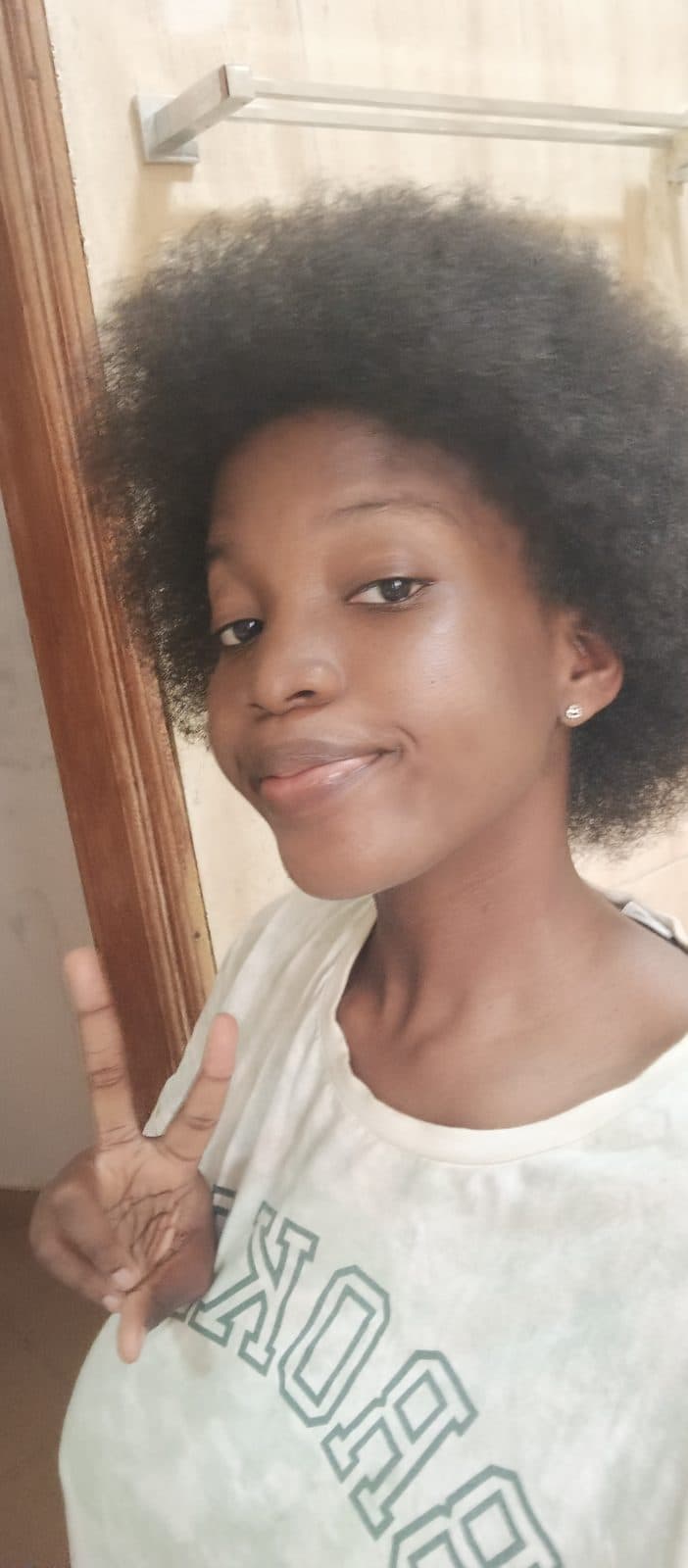 Omotola en gros plan, cheveux afro et t-shirt blanc, un sourire retenu.