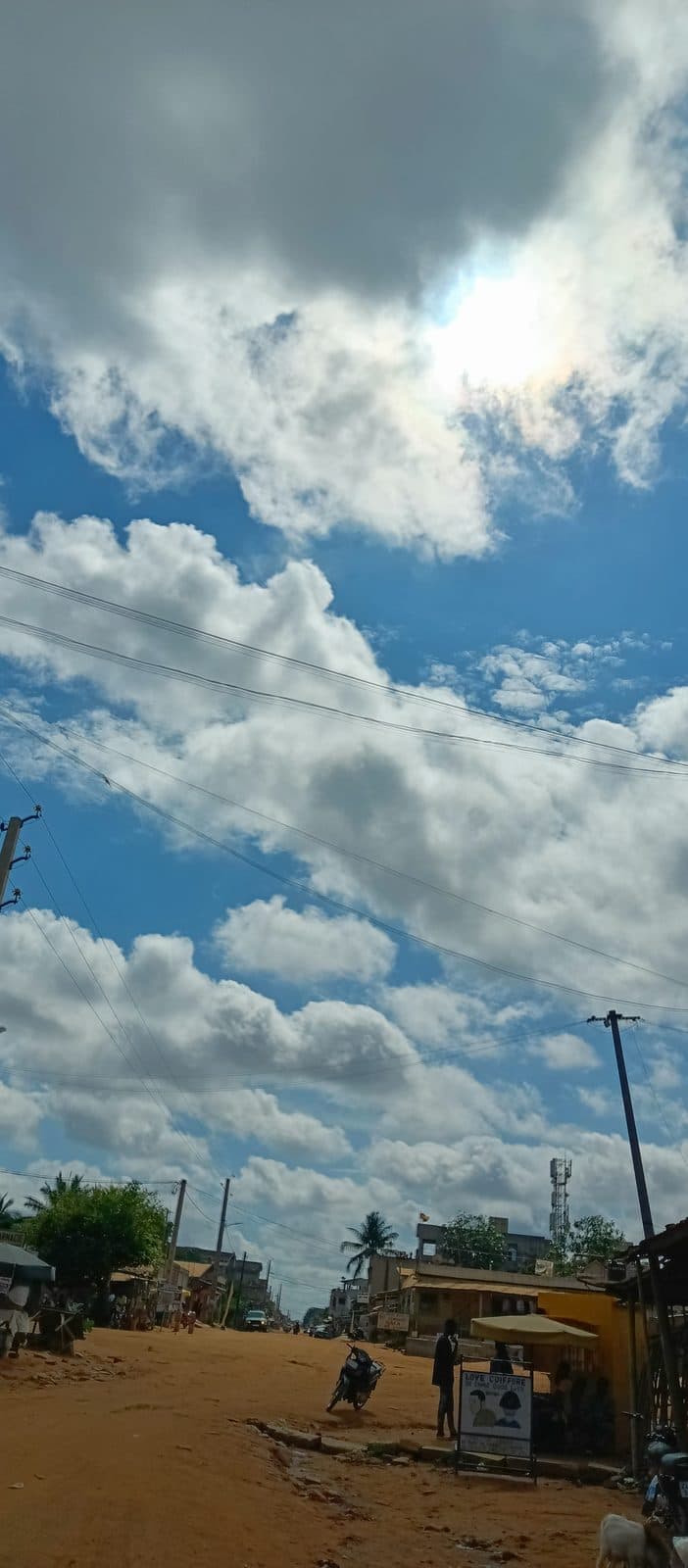 Une rue de Cotonou sous un grand ciel de nuages, en fin de journée.