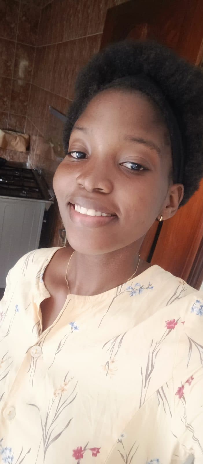 Omotola souriante, en haut à fleurs, dans une pièce claire.