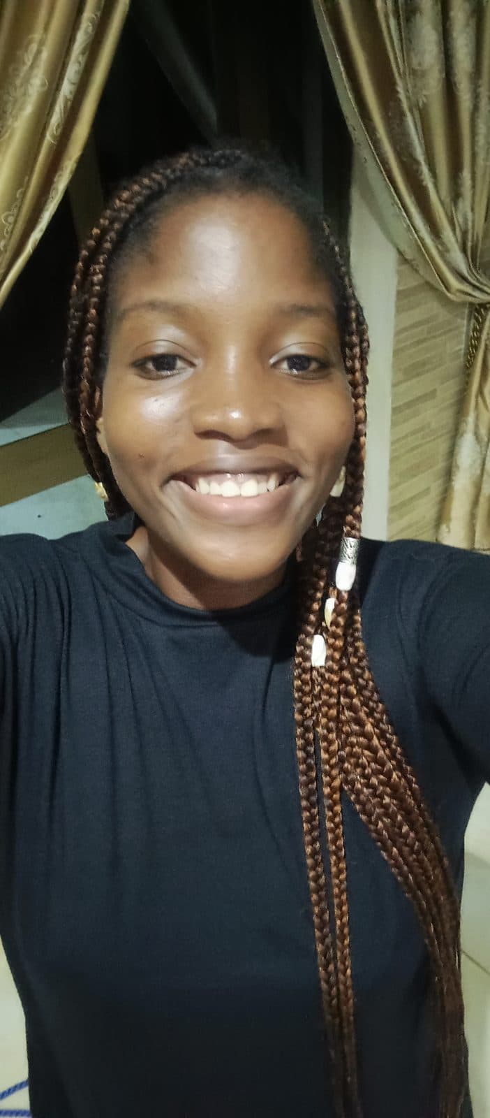 Omotola souriante, en haut noir, ses longues tresses ramenées sur l’épaule.