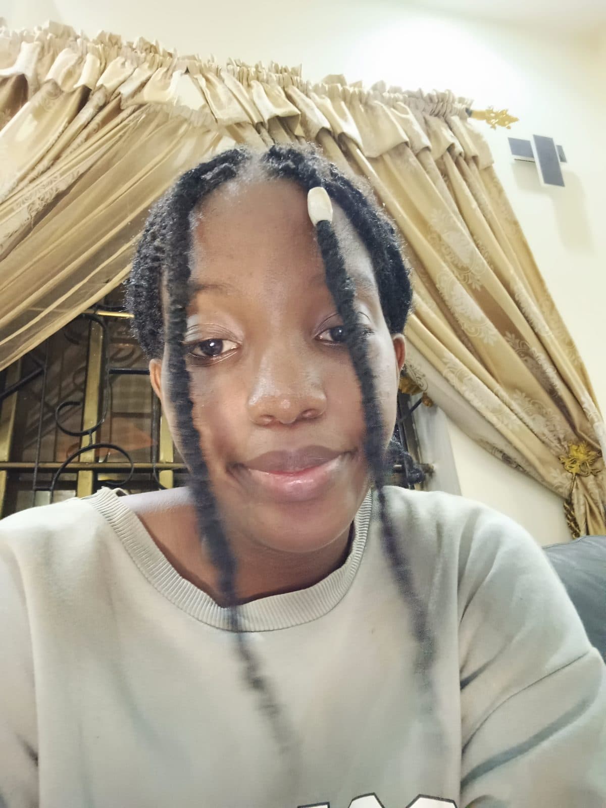 Omotola de face, longues tresses, devant un rideau clair.