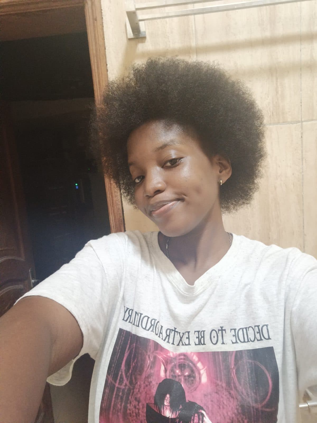 Omotola en extérieur, cheveux afro et t-shirt imprimé.