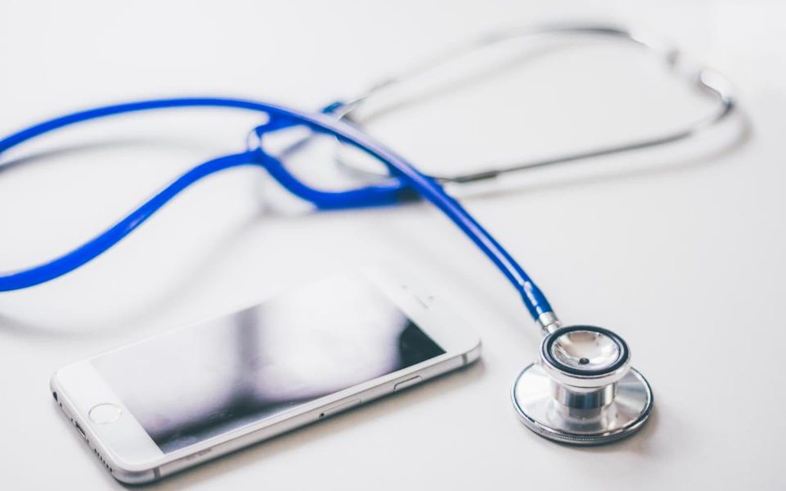 Un stéthoscope posé à côté d’un téléphone, sur une table blanche.