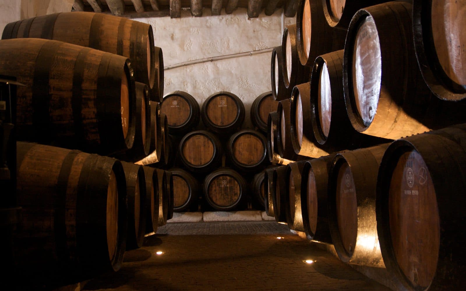 Des tonneaux de vin empilés dans une cave voûtée.