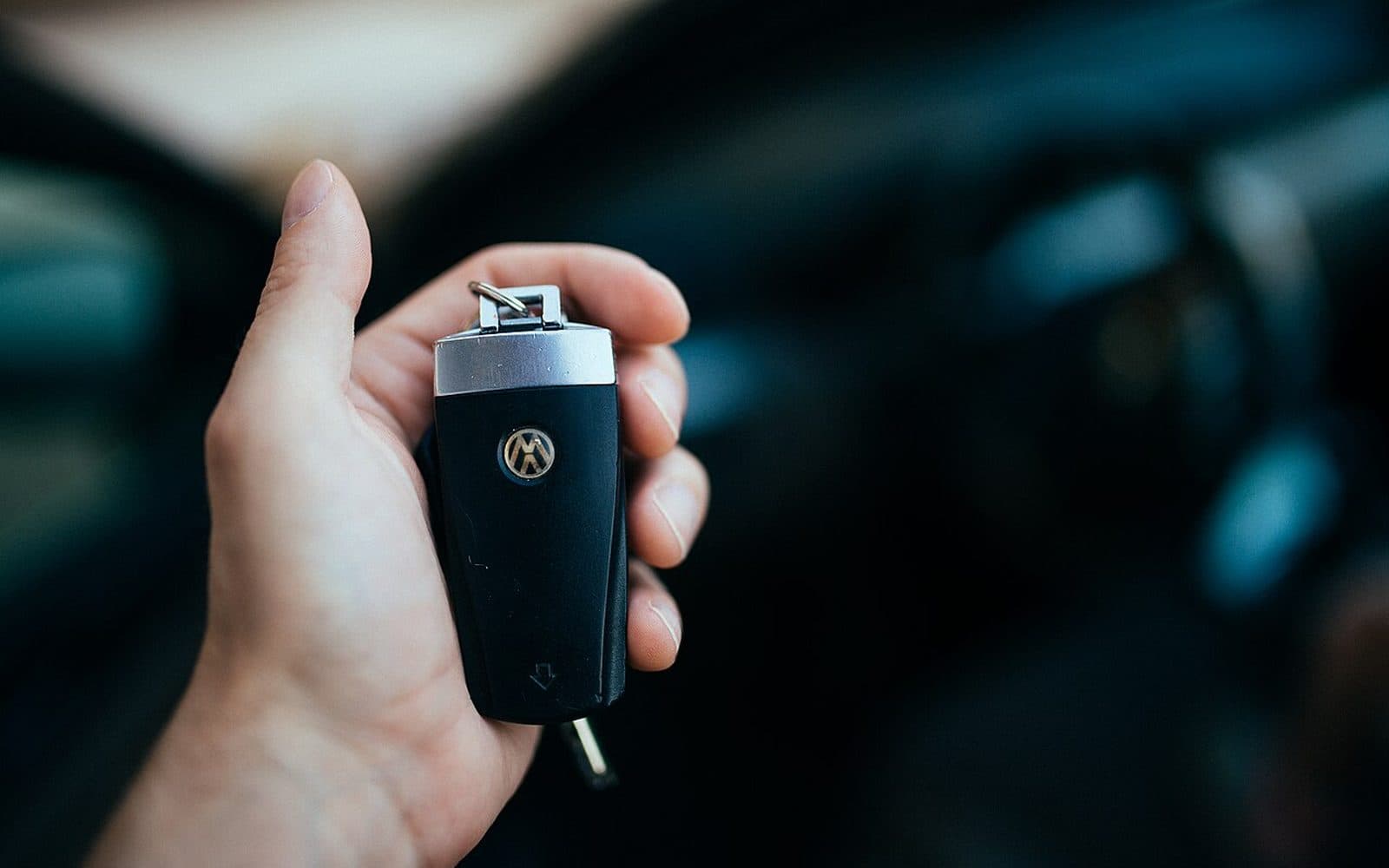 Une main tend une clé de voiture, la voiture floue à l’arrière-plan.
